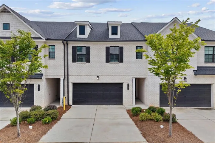 White brick exterior with black shutters, dark garage doors, dormer windows, and established landscaping