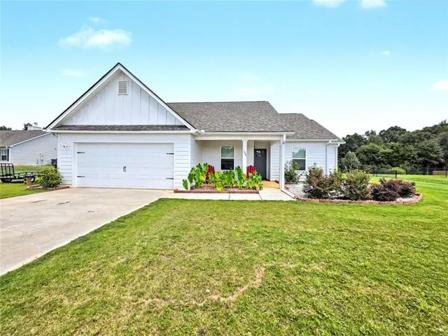 Single-story residence featuring white siding, an attached garage, a covered entry, and established landscaping