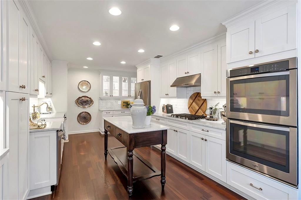 Kitchen featuring dark wood-type flooring, stainless steel appliances, light stone counters, and white cabinets