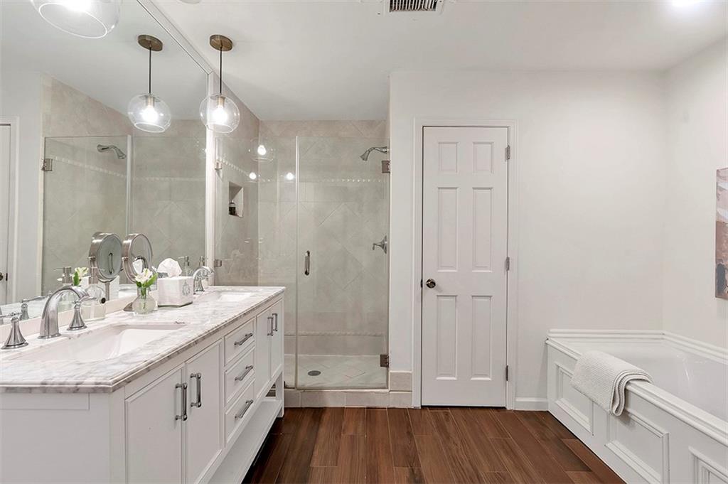 Bathroom with large vanity, independent shower and bath, wood-type flooring, and double sink