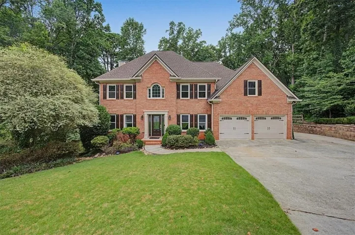 Traditional brick two-story residence featuring a prominent arched window, dark paneled shutters, a stone-accented entry, and a two-car garage