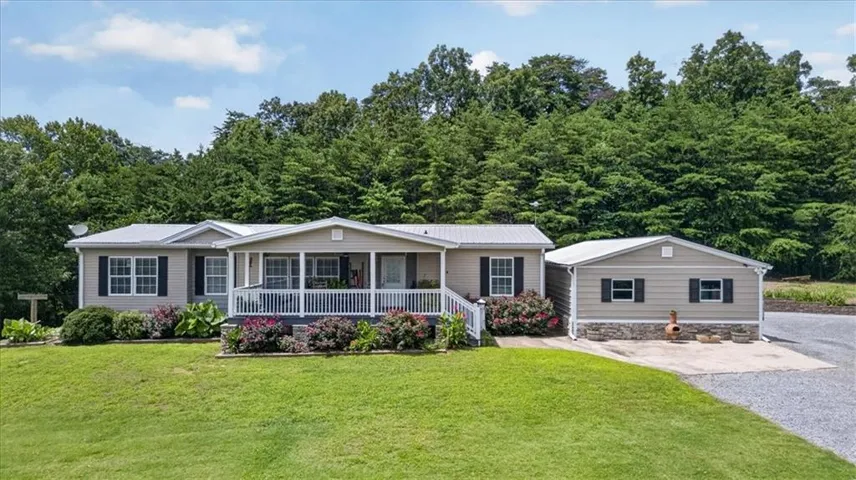 Ranch-style residence featuring a metal roof, a covered front porch with white railings, and a detached structure with a stone-finish base