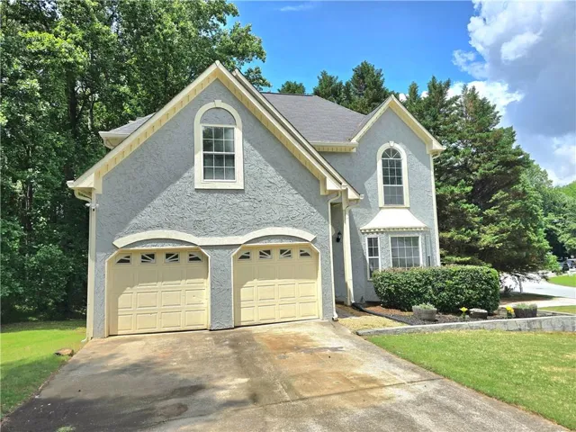 Stucco exterior with decorative trim, arched window, bay window, dual garage doors, and mature landscaping