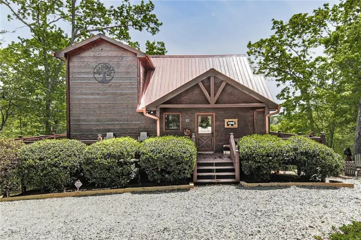Charming rustic cabin exterior with wood siding and a metal roof, featuring a welcoming covered front porch and a private wooded setting.