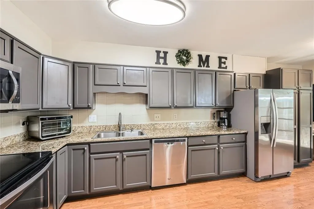 Kitchen featuring gray cabinetry, appliances with stainless steel finishes, tasteful backsplash, light wood-style flooring, and light stone countertops