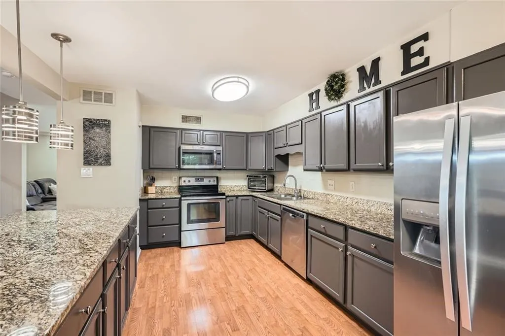 Kitchen with stainless steel appliances, light wood-style floors, decorative light fixtures, gray cabinetry, and light stone countertops