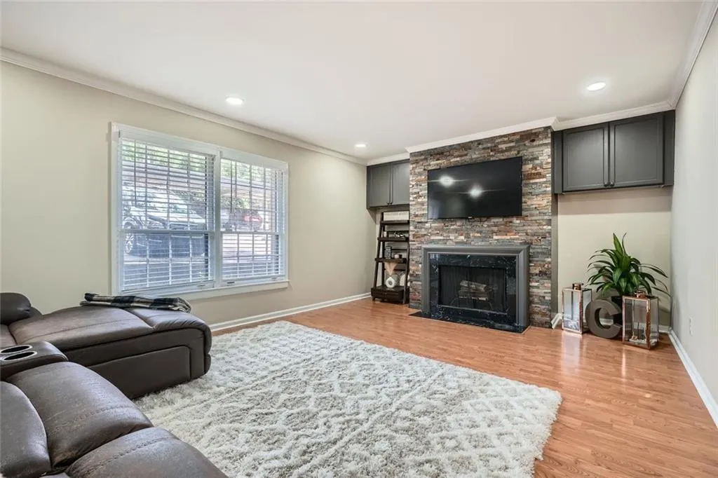 Living room featuring ornamental molding, light wood finished floors, a stone fireplace, and recessed lighting