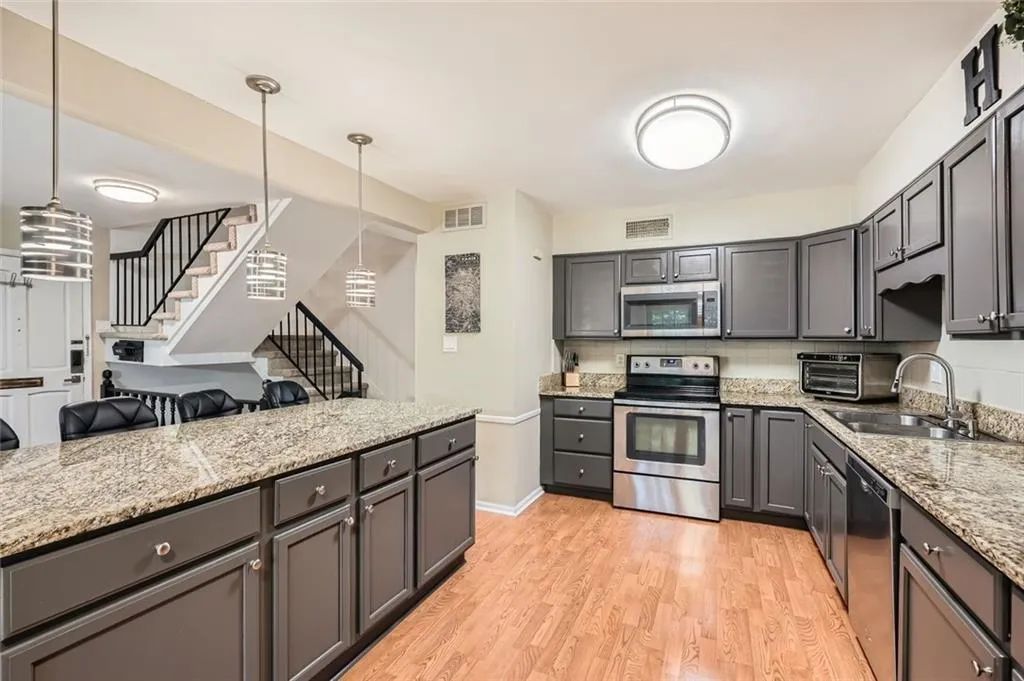 Kitchen with stainless steel appliances, gray cabinets, light wood-style flooring, hanging light fixtures, and light stone counters