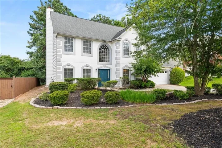 Stately two-story residence featuring a white facade with gray architectural accents, an arched window, and a vibrant blue entry door