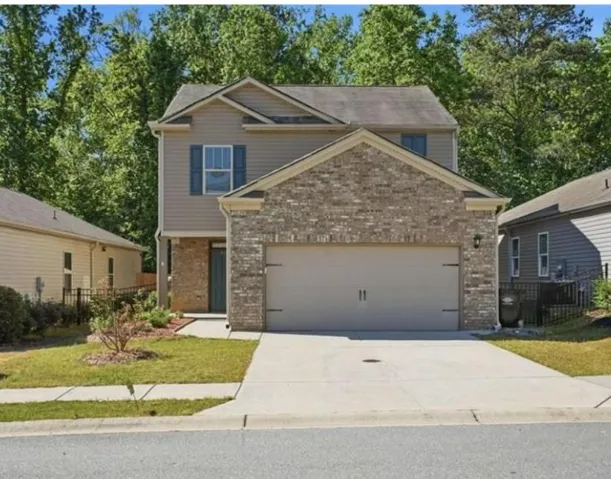 Two-story residential structure featuring brick and siding facade, an attached garage, a paved driveway, and a front lawn with foundational landscaping