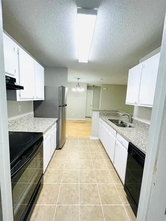 Kitchen featuring a sink, a textured ceiling, black appliances, white cabinetry, and under cabinet range hood