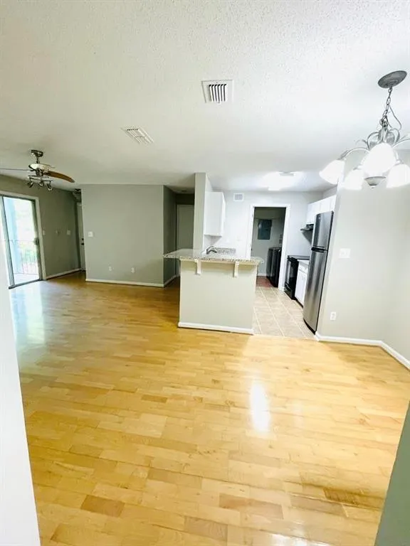 Unfurnished living room featuring baseboards, visible vents, a textured ceiling, and light wood-style floors