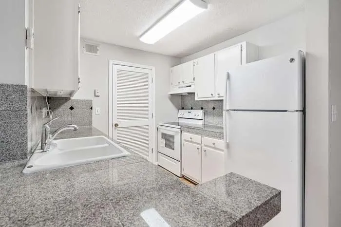 Kitchen featuring a sink, backsplash, white cabinetry, white appliances, and under cabinet range hood