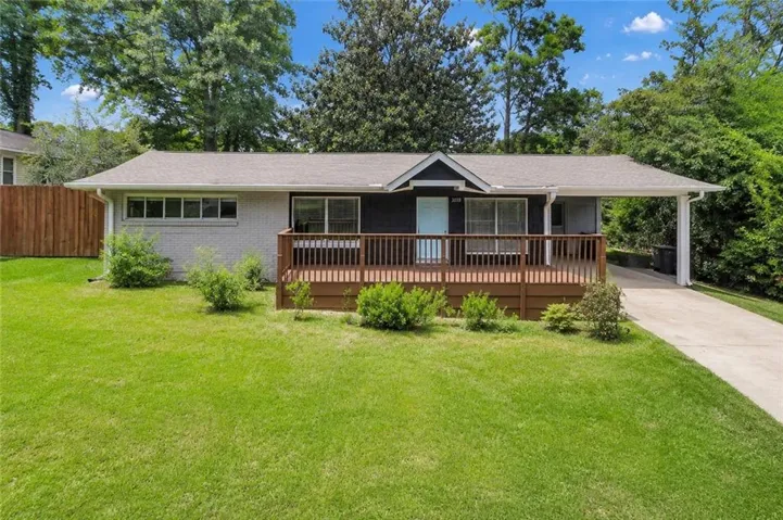 Light gray brick exterior with a dark-painted facade, featuring a wide front deck with wood railing, a carport, and a concrete driveway