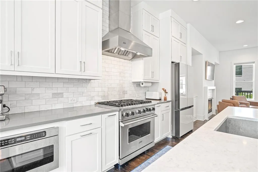Kitchen featuring wall chimney range hood, white cabinetry, stainless steel appliances, dark wood finished floors, and light stone counters