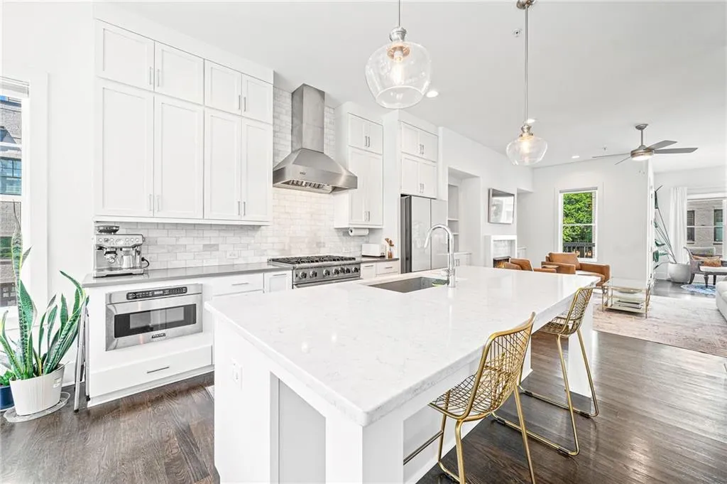 Kitchen with white cabinets, a kitchen bar, backsplash, decorative light fixtures, and wall chimney exhaust hood
