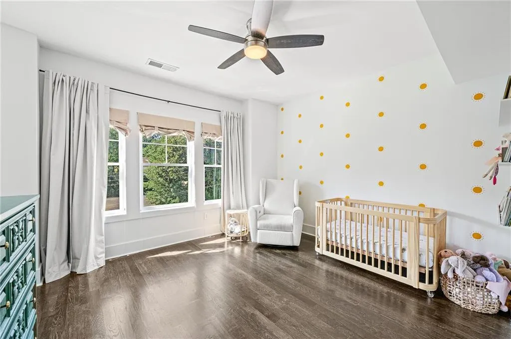 Bedroom featuring dark wood-type flooring, a nursery area, and a ceiling fan