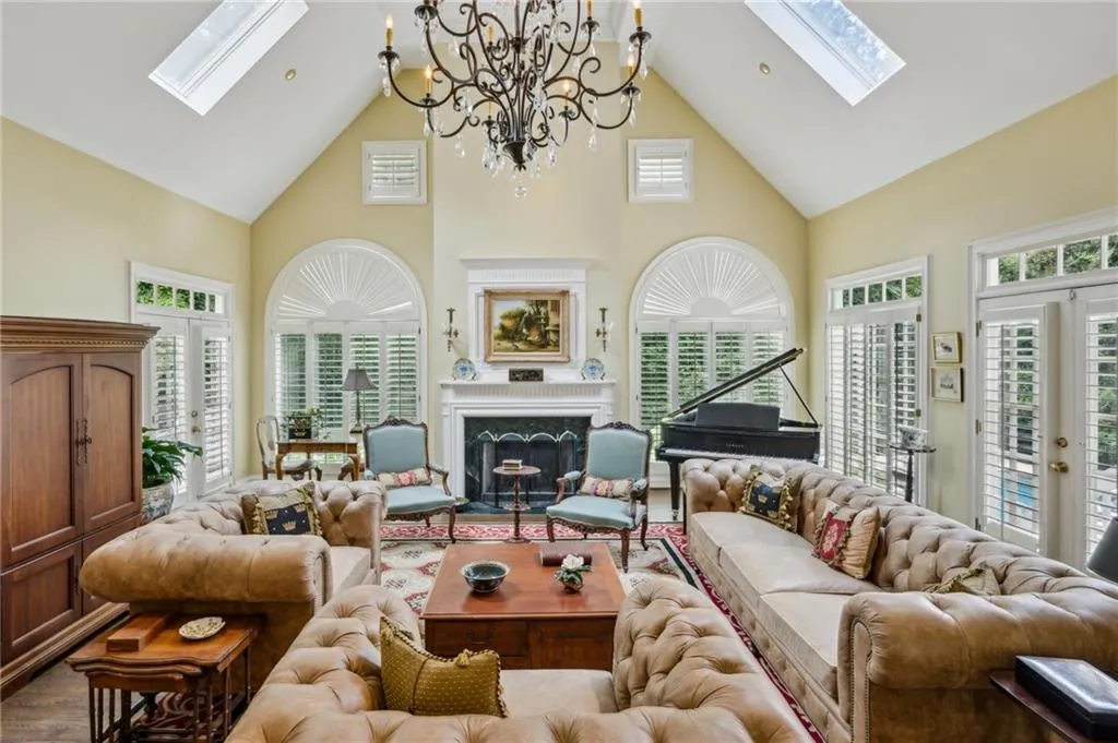 Bright great room with dramatic two-story vaulted ceiling, skylights, French doors, and fireplace