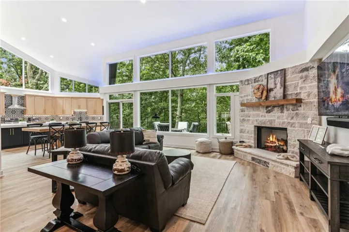 Living area featuring a high ceiling, a stone fireplace, light wood finished floors, and recessed lighting
