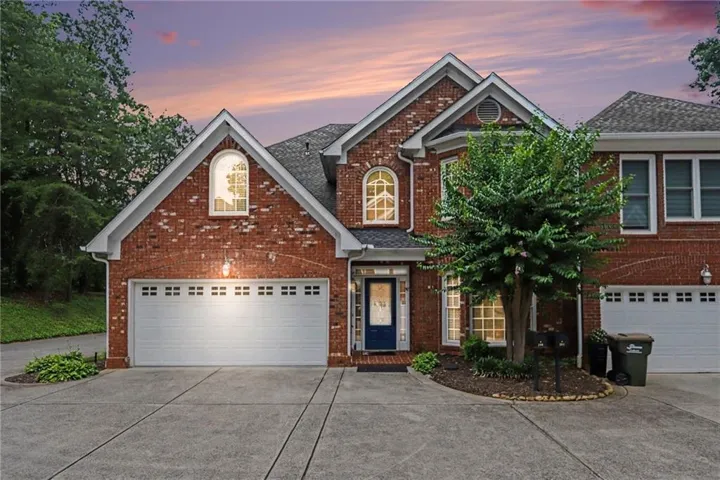 Brick facade residence featuring multiple gables, arched windows, a dark blue entry door, and a two-car garage