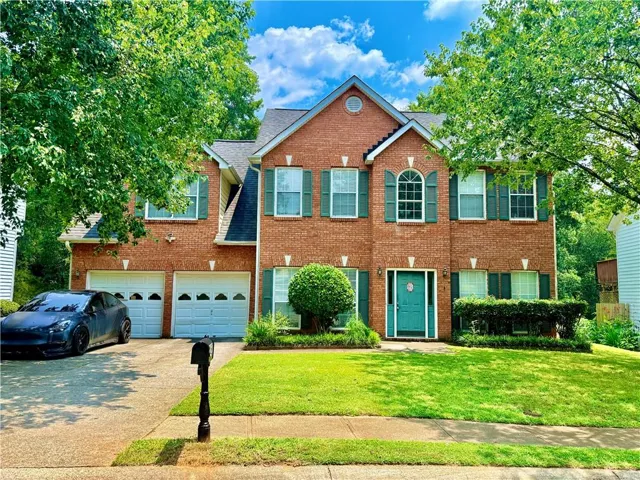 Brick exterior residence featuring a two-story design, a two-car garage, a prominent arched window, and a vibrant teal entry door