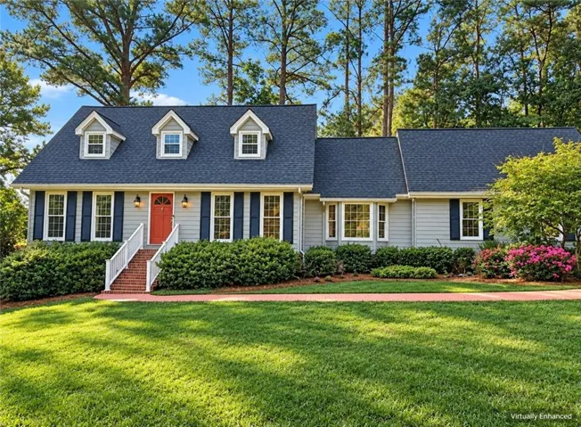 Gable roofline with three dormer windows, red entry door, bay window, dark shutters, and mature landscaping
