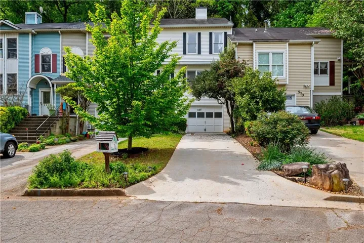 Multi-level townhome with a light-colored facade, attached garage, and a concrete driveway