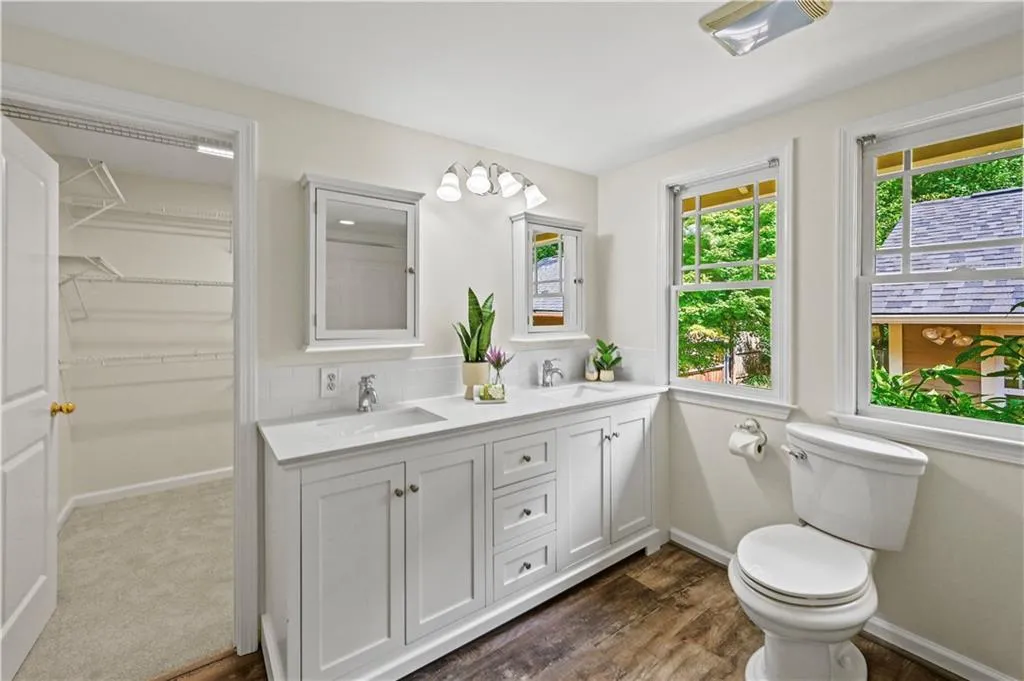 Bathroom featuring double vanity, dark wood finished floors, a spacious closet, and tasteful backsplash