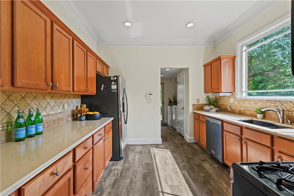 Kitchen with backsplash, ornamental molding, dark wood-style flooring, brown cabinets, and washer and dryer