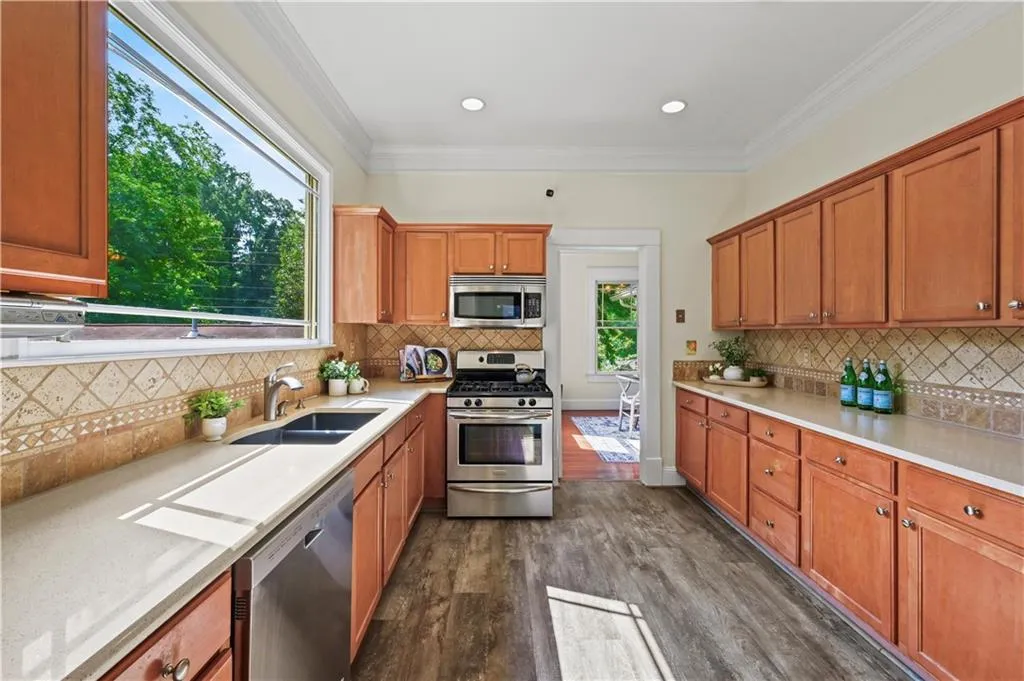 Kitchen with stainless steel appliances, dark wood finished floors, crown molding, brown cabinets, and decorative backsplash