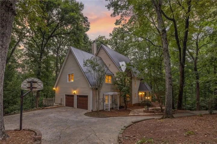 Wooded lot with a substantial multi-level residence featuring a metal roof, two-car garage with wood-paneled doors, and a stone-paved walkway