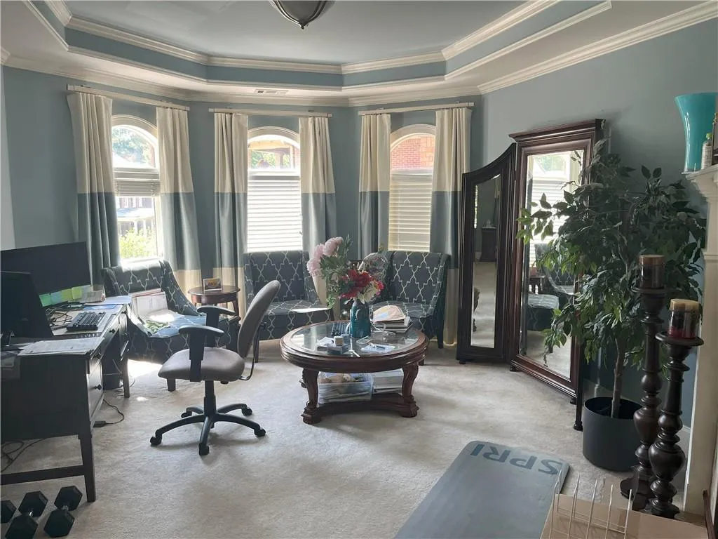 Living area featuring a tray ceiling, carpet flooring, a desk, and ornamental molding