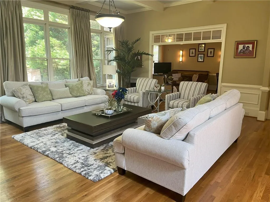 Living area featuring beam ceiling, wood finished floors, ornamental molding, and a wainscoted wall