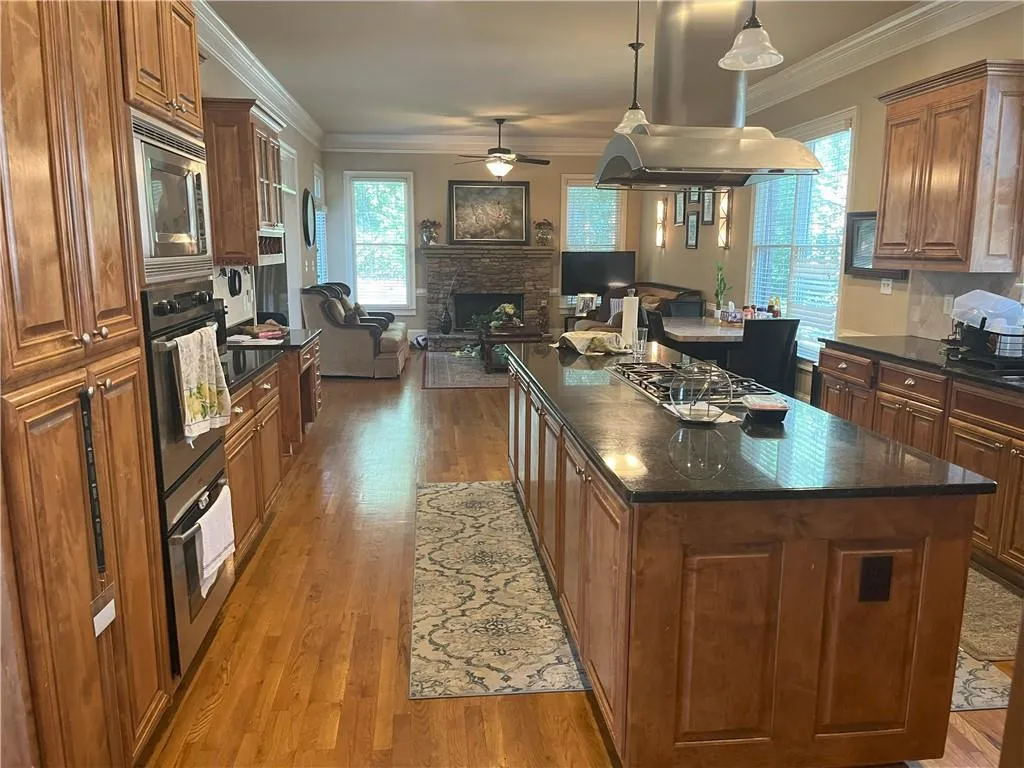 Kitchen featuring ornamental molding, brown cabinetry, island exhaust hood, a center island, and light wood finished floors