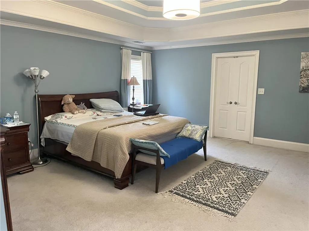 Bedroom with light carpet, crown molding, a tray ceiling, and a closet