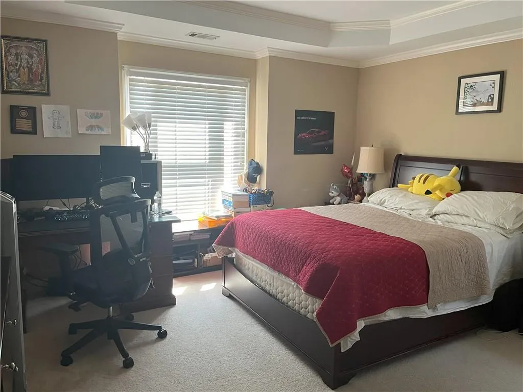 Carpeted bedroom featuring a raised ceiling, crown molding, and an office area