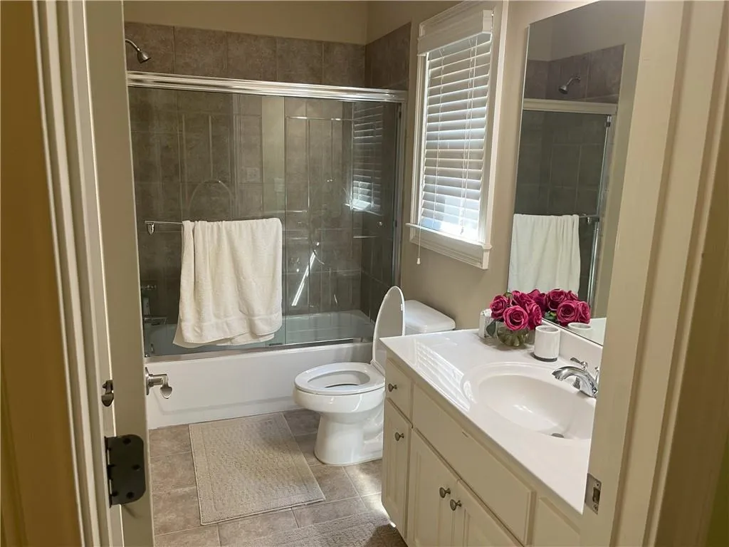 Bathroom featuring shower / bath combination with glass door, vanity, and light tile patterned floors