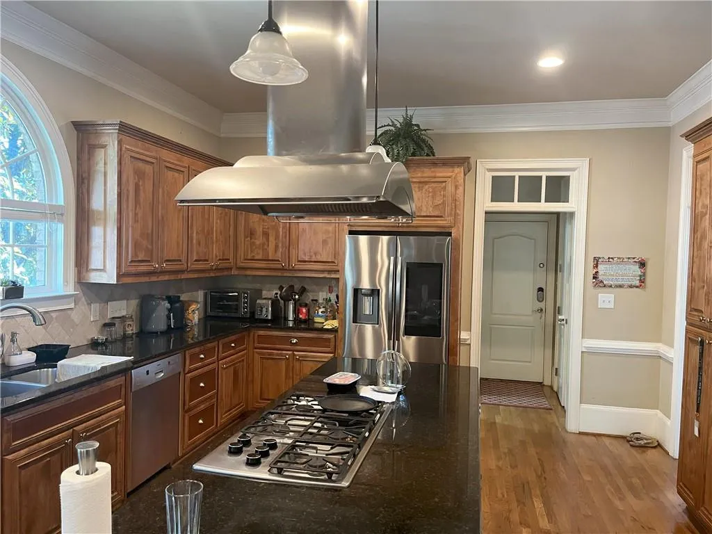 Kitchen featuring crown molding, decorative backsplash, dark stone counters, island range hood, and stainless steel appliances