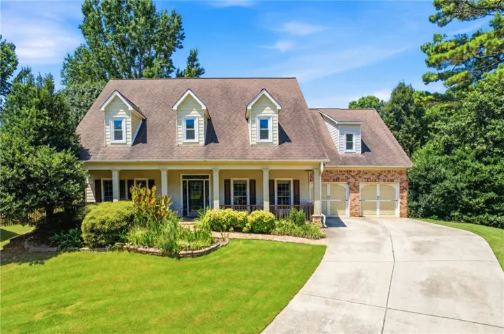 Traditional-style residence featuring a dormered roofline, a columned front porch, and a two-car garage with brick veneer
