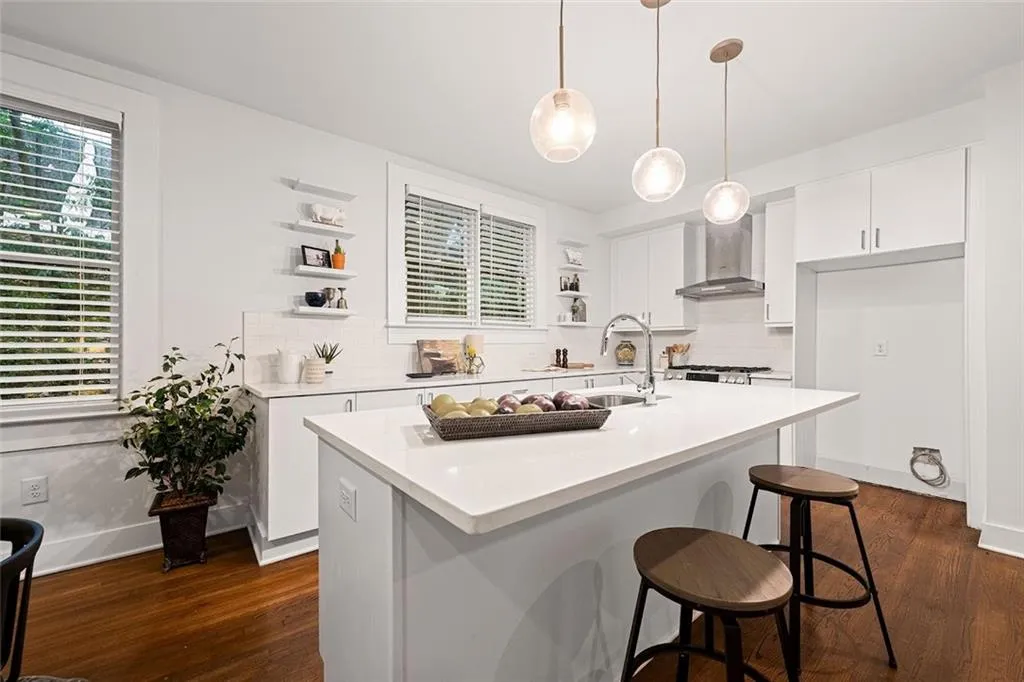 Kitchen featuring a kitchen island with sink, wall chimney exhaust hood, white cabinetry, and dark hardwood / wood-style floors