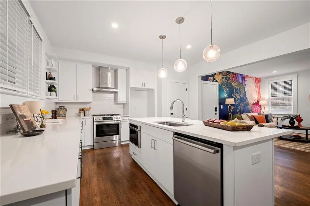 Kitchen with a kitchen island, wall chimney exhaust hood, pendant lighting, appliances with stainless steel finishes, and sink