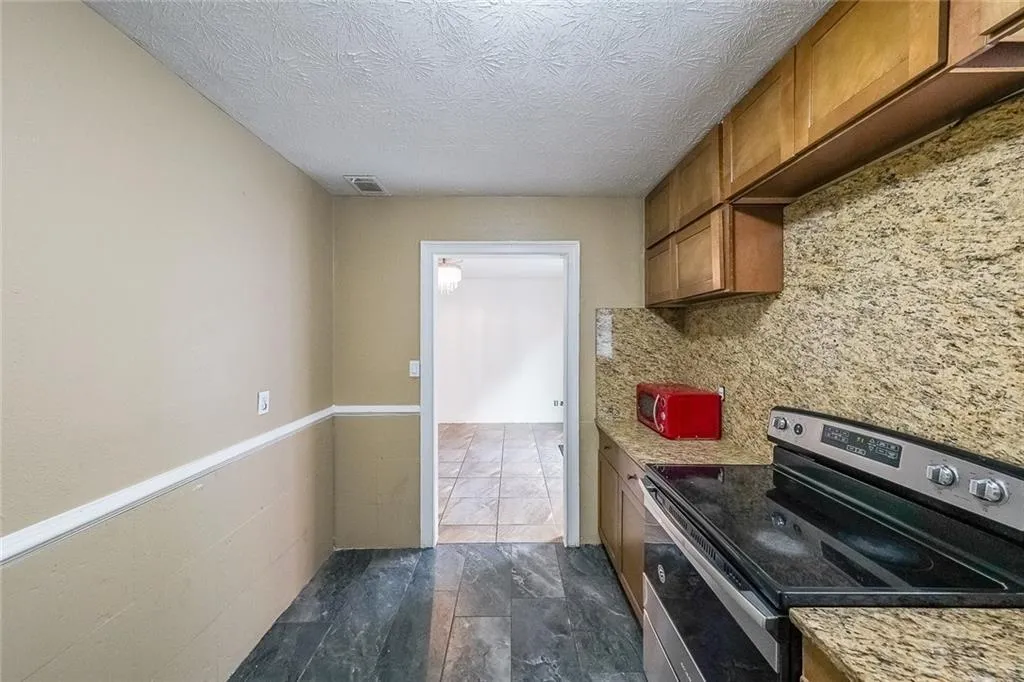 Kitchen with stainless steel electric stove, brown cabinets, decorative backsplash, and a textured ceiling