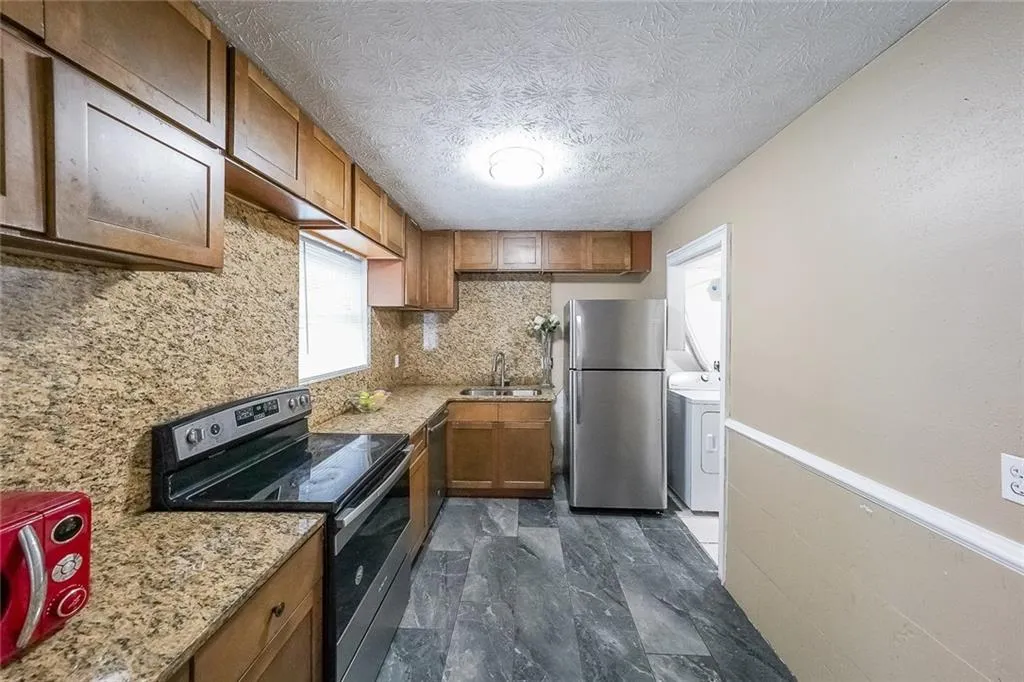 Kitchen featuring stainless steel appliances, washer / clothes dryer, a textured ceiling, brown cabinets, and decorative backsplash