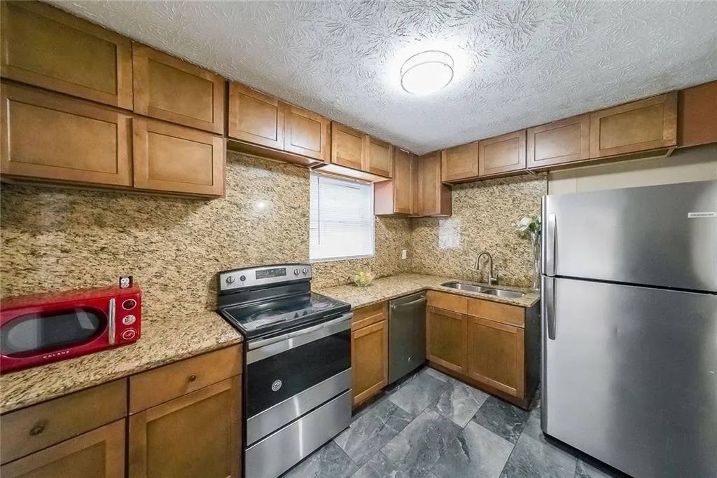Kitchen with stainless steel appliances, brown cabinets, light stone counters, decorative backsplash, and a textured ceiling