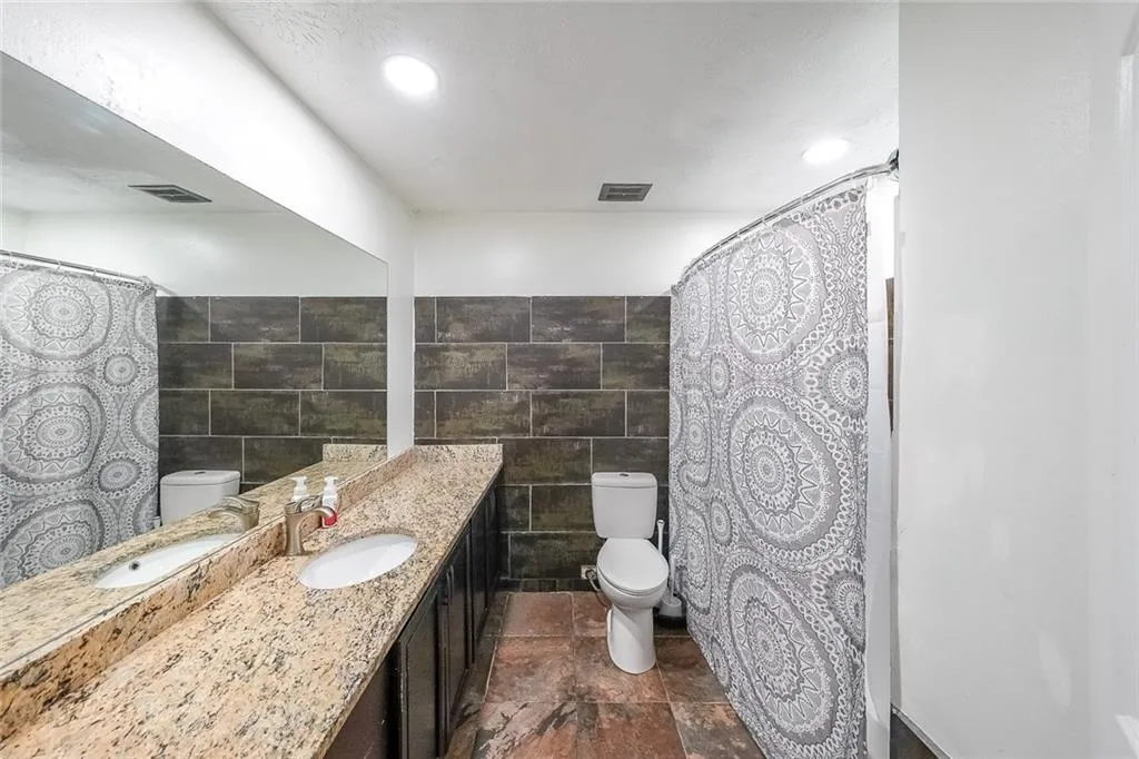 Bathroom with a shower with shower curtain, stone tile floors, vanity, tile walls, and recessed lighting