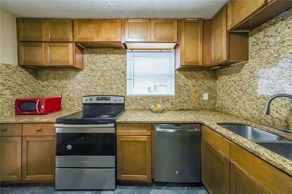 Kitchen featuring stainless steel appliances, brown cabinetry, and light stone counters