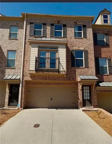 Brick townhouse facade with a two-car garage, upper-level balcony, and window shutters