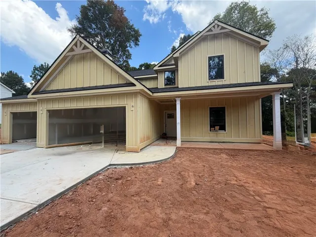 Two-story residence featuring board and batten style siding, an attached two-car garage, a covered front porch, and black-framed windows