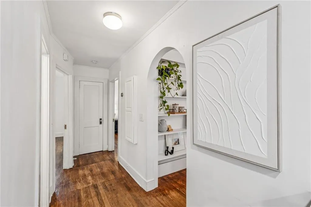 Hallway featuring dark wood-style floors, crown molding, and arched walkways