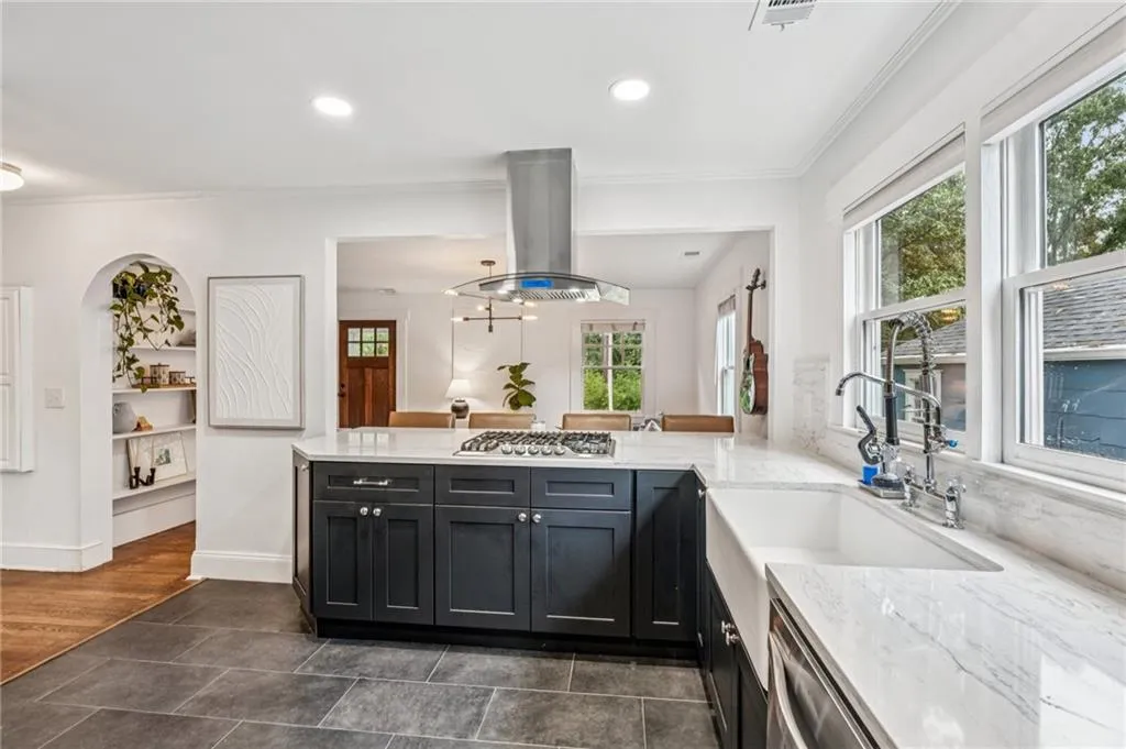 Kitchen featuring light stone countertops, dark cabinetry, island range hood, a peninsula, and recessed lighting